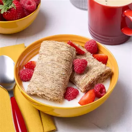 Shredded Wheat Original Bowlshot in a yellow bowl with a spoon and cup of tea
