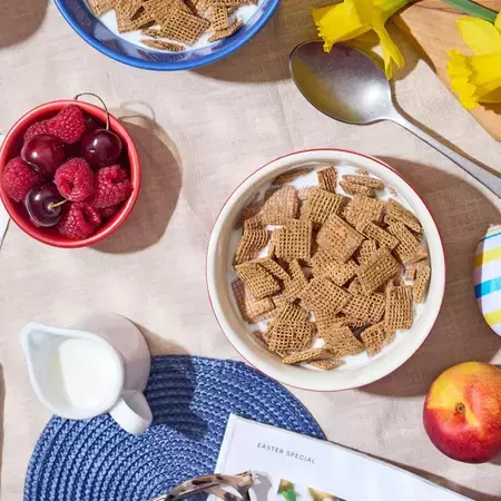 Shreddies in a white bowl, on a spring breakfast table with milk, berries and daffodils